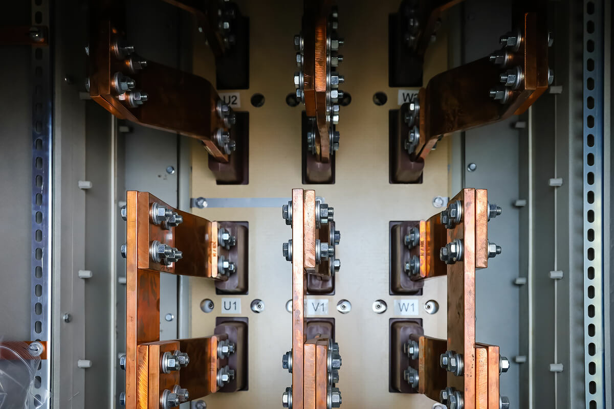 Copper bus bars bolted to labeled three-phase terminals inside an electrical switchgear cabinet